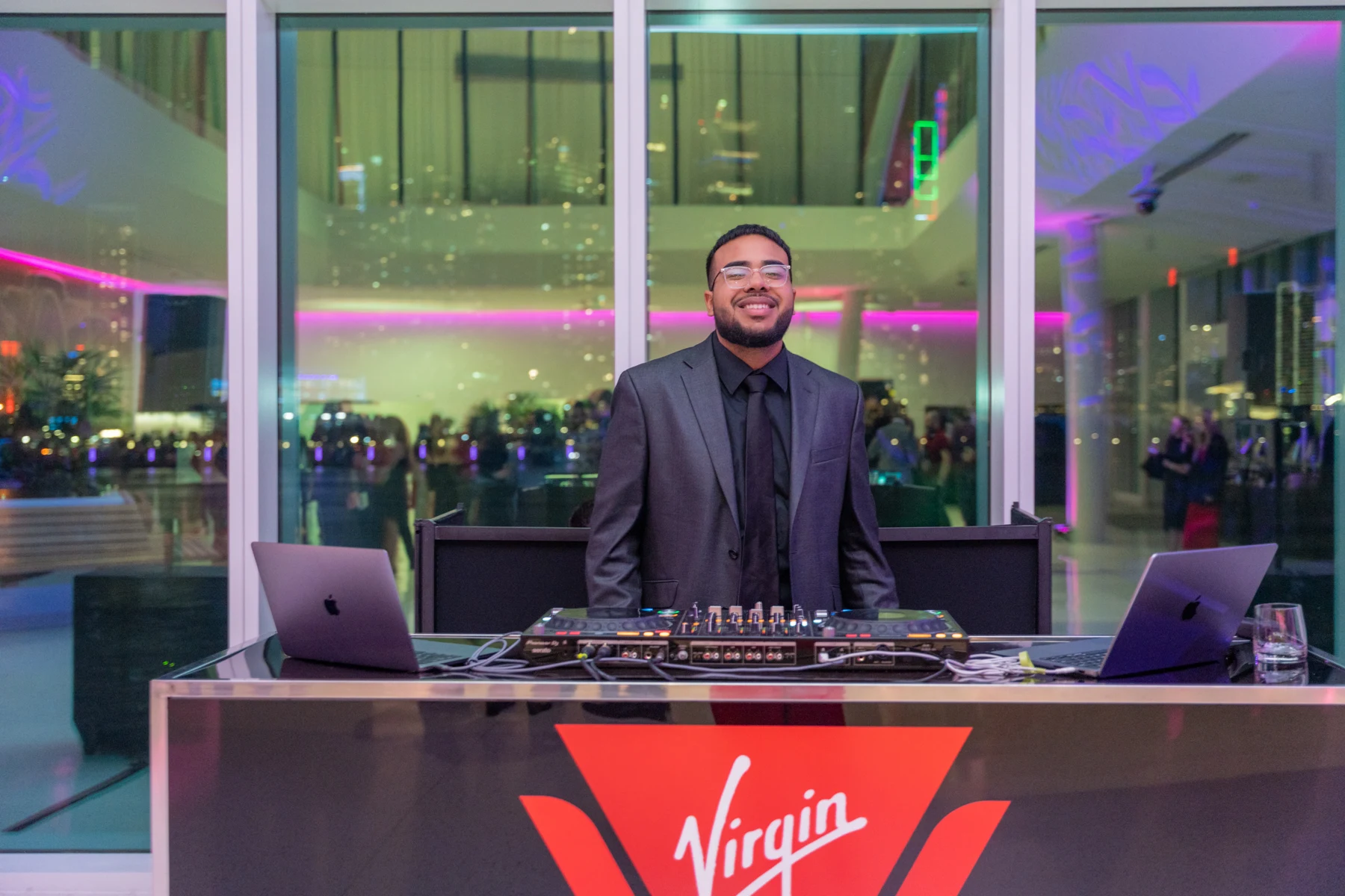 A DJ behind a branded booth with purple lighting