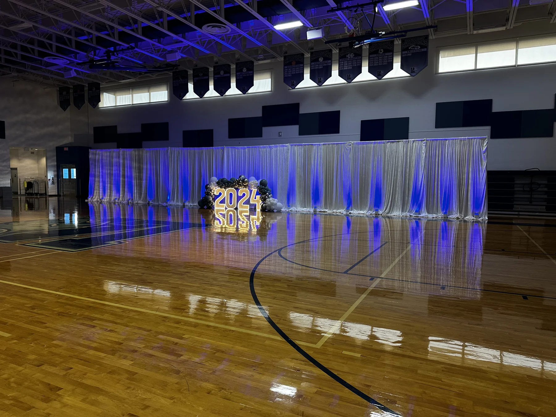 White event draping and blue uplighting across a gymnasium