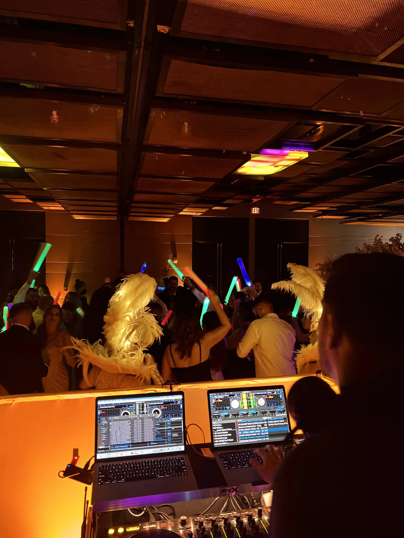 A DJ overseeing a dance floor with light-up props and feathered performers