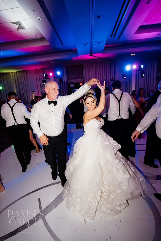 A bride and groom dancing beneath event lighting
